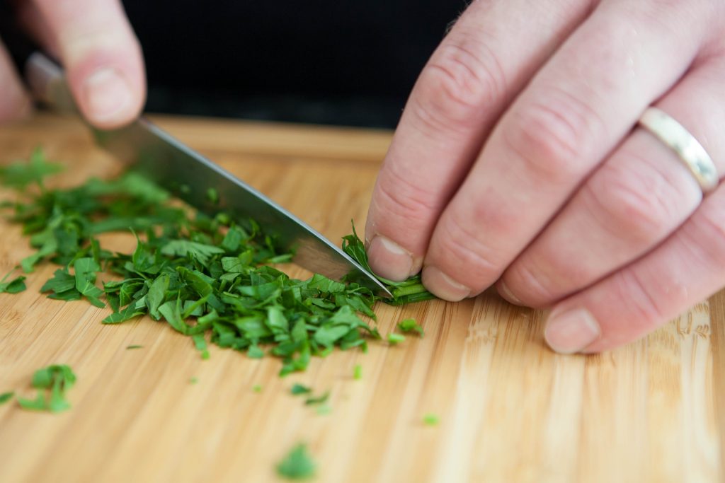 Hands holding a knife while cutting parsley